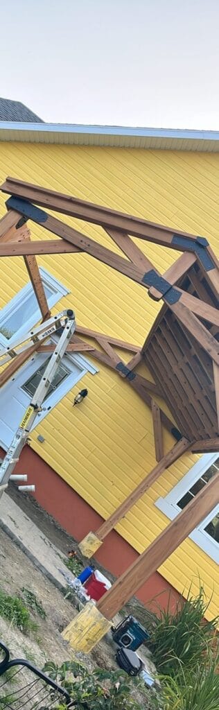 Pergola en bois assemblée contre une maison jaune